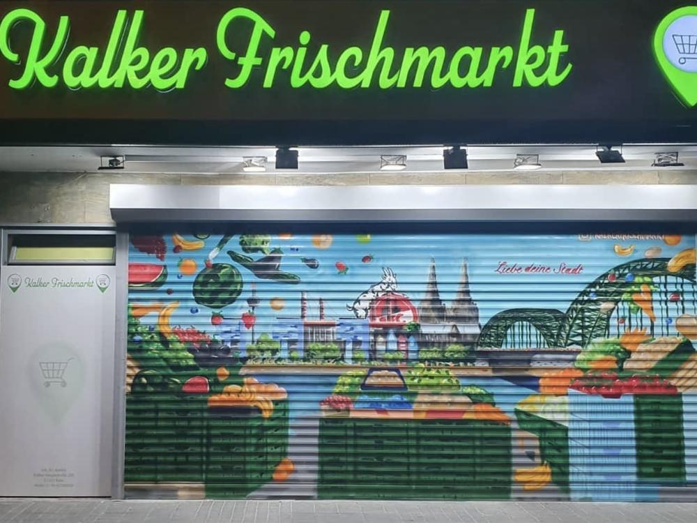 Der Kalker Frischmarkt bei Nacht mit beleuchtetem Schriftzug und bemaltem Rolltor
